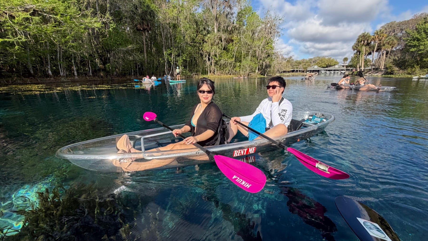 Two guests paddling a transparent tandem kayak with pink paddles