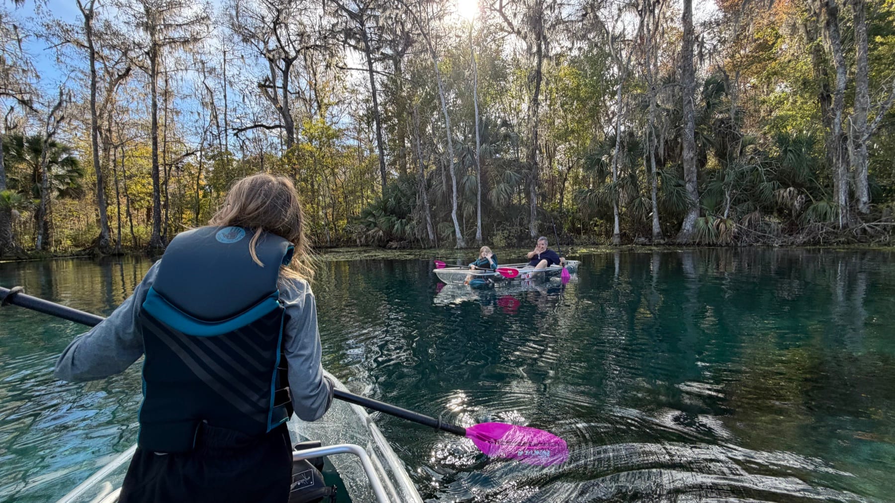 Guests paddling clear kayaks along a shaded spring river